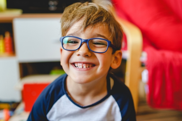 Portrait of happy caucasian boy with eyeglasses sitting at home in room in day real people small male playful child looking to the camera smiling