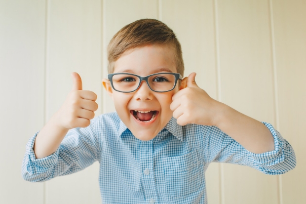 A child with glasses gives a thumbs-up. A kid likes the glasses. Little boy approves.