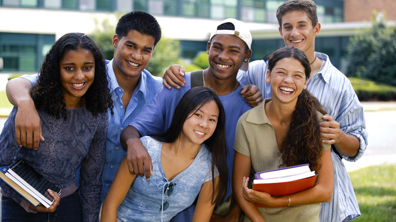 A multi-ethnic goup of young adults smiling and holding books