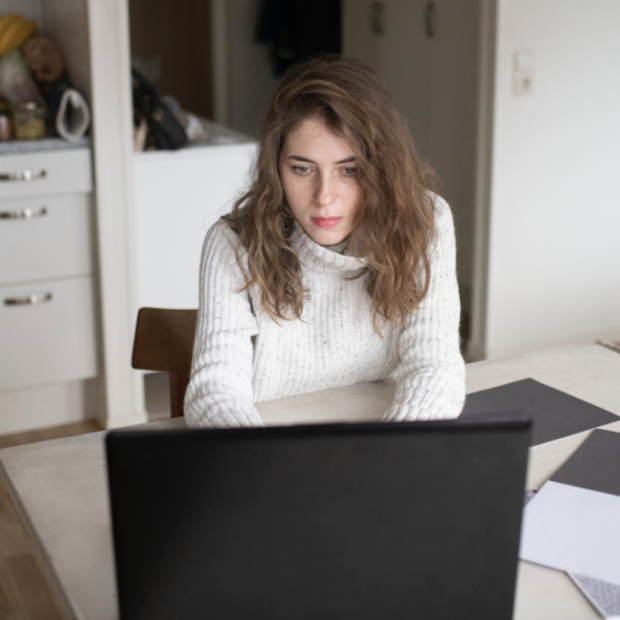 Woman in white sweater looks at computer screen image from Well + Good