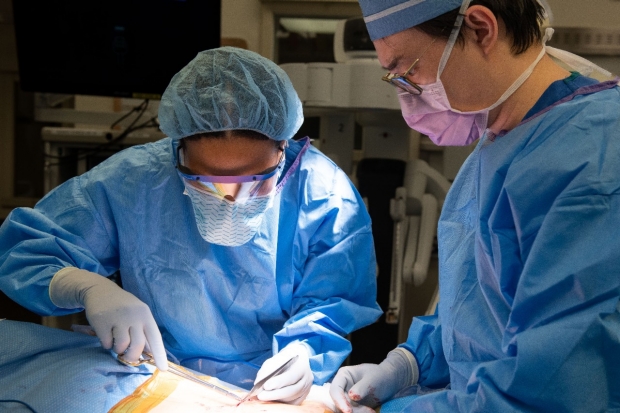A medical student sutures an incision closed under the tutelage of Resident Dr. Jeff Choi. 