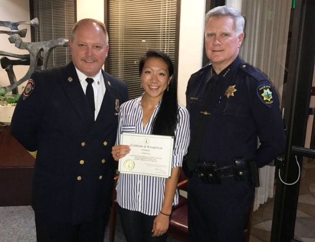 Two fire officials standing next to a medical student holding a certificate