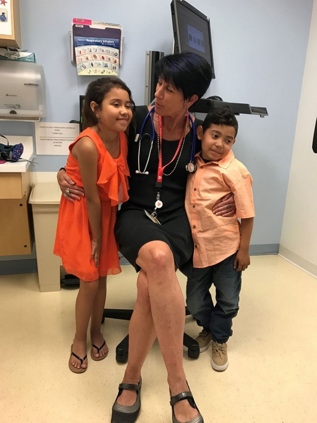Woman sitting in a patient exam room with her arms around a young girl and a young boy