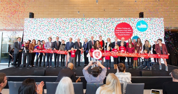 People lined up to cut a large ribbon with a confetti banner behind them