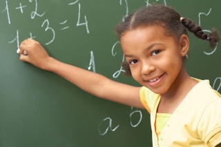 Happy young girl doing math on a chalkboard