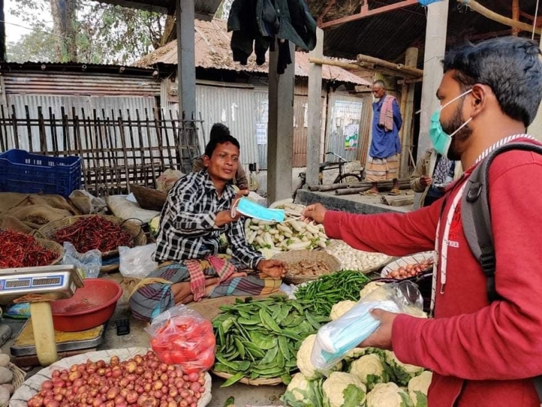 Providing a woman with a surgical mask at a market in Bangladesh 