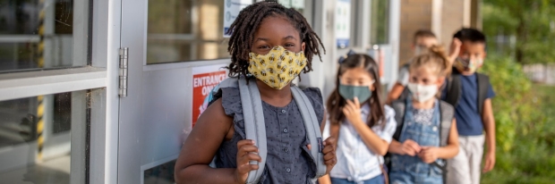 Diverse school-aged children in masks outside of school from iStock Getty Images